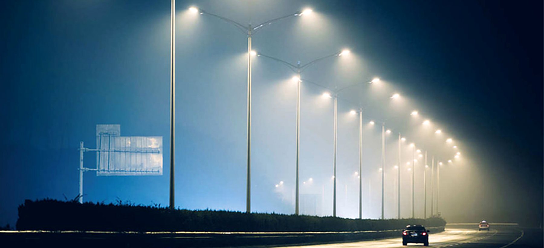 A highway at night lit by a receding row of street lighting poles